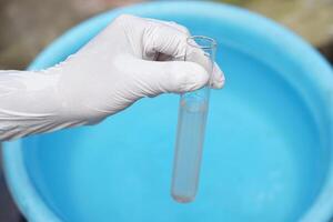 Close up ecologist hand wears glove holds test tube of water. Concept, Inspecting water quality from nature source that use in daily life. Examination water pollution. Environmental problems. photo