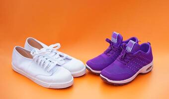 Two pairs of white and purple canvas sneakers. Orange background. Comfortable, fashionable. Concept, shoes for doing sport or exercise also can wear for traveling, hiking. photo