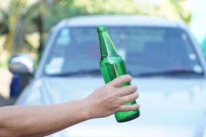 cerca arriba mano sostener botella de cerveza, exterior, borroso coche antecedentes. concepto, detener conducción mientras Bebiendo alcohol bebida o whisky campaña. ilegal, peligroso a conducir vehículo ese dirigir a accidente foto