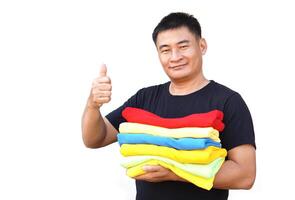 Handsome Asian man hold folded colorful clothes, thumbs up. White background. Concept, daily chore, household. Folded clothes for neat and clean. Maintenance and keep garments for sanitary. photo