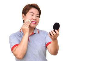 Asian middle aged woman is making up, using puff to apply powder on her face, looking at portable mirror Concept, women don't stop beauty, using cosmetics. Woman lifestyle, make self always looks good photo