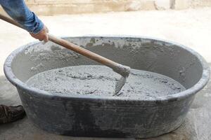 cerca arriba trabajador utilizando un azada a mezcla cemento polvo, arena, piedras en cuenca para mezcla cemento. concepto. construcción trabajador trabajo. difícil laboral. proceso de construcción trabajo con cemento foto