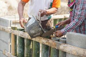 Close up workers help each other to pour cement into bamboo molding for building at construction site. Concept. Construction worker job. Hard working. Process of construction work with cement photo