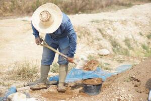 Asian worker man is digging sand into bucket for mixing with cement powder in construction work, outdoor. Concept, labour, builder occupation. Hard working in hot weather, risk to heat stroke. photo