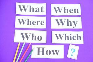 Paper cards with Wh-question words and question marks on purple background. Concept. Teaching aid. Education materials for teach WH- question. Asking questions. Suspicious symbol to find answer. photo