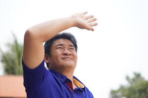 Asian man is outdoor, face up to sky, hand over his head, feel hot and unwell. Concept, standing outdoor in hot weather is risk to heat stroke symptom. Global warming. photo