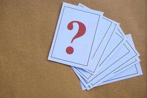 Overlapped pile of paper cards of question mark on brown background. Concept. Teaching aid. Education materials for doing activity or playing games about find answers. photo