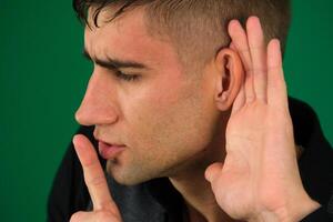 oye por casualidad un hombre, intentos a escuchar. emociones de un hermoso hombre chico en un verde antecedentes chromakey de cerca oscuro pelo joven hombre foto