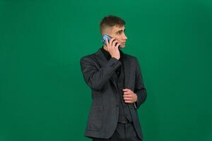 A man vaping in formal suit emotions of a handsome man guy on a green background chromakey close-up dark hair young man. phone in hand talk dial SMS online call gadget boss work advertising photo