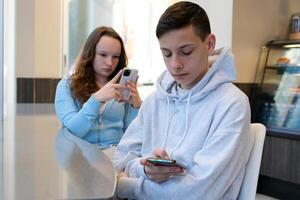 teenagers on date hold phones in hands are busy in social networks do not see each other Bored attractive woman looking tired while boyfriend uses a smartphone to record a short story for social media photo