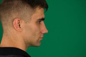 Close up profile view of young handsome man isolated against emotions of a handsome man guy on a green background chromakey close-up dark hair young man photo