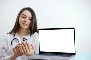 Happy smiling female doctor pointing at tablet pc with empty copy space area for slogan or text over office white brick loft wall. Medical call center concept. Zoom online consult. iPad touchpad photo