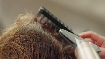 uma cabeleireiro faz uma mulher cabelo dentro uma beleza salão com uma cabelo secador e uma pentear. mulheres beleza Cuidado. Alto qualidade 4k cenas video