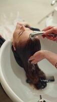 fermer de une salon de coiffure mains la lessive une femme cheveux. le travail de une professionnel est confort à le beauté procédures dans le salon. haute qualité 4k métrage video