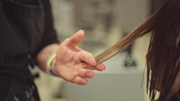 Close-up of a hairdresser's hand cutting a woman's hair with scissors. Hairstyle and haircut in a beauty salon by a professional. High quality 4k footage video