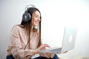 niña con ordenador portátil auriculares felizmente relojes película escucha a música estudiando en línea conferencia comunicación con amigos teniendo divertido en un blanco antecedentes publicidad un en línea formación curso o trabajo foto