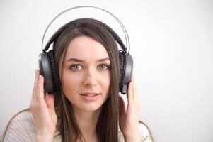 Smiling girl relaxing at home, she is playing music using a smartphone and wearing white headphones photo