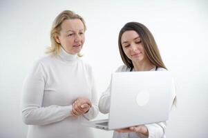 young girl doctor shows tests on a laptop to an adult woman in white clothes on a white background advertising a good medicine helping patients care internet consultation online hospital polyclinic photo