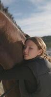 un niña abrazos y golpes un caballo en un rancho. un estilo de vida de amor y cuidado para animales, aprendizaje a paseo un caballo. alto calidad 4k imágenes video