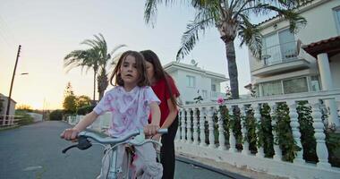 Happy childhood, mother teaches daughter to ride a bicycle. lifestyle, a woman supports a bicycle to a girl who rides, parental help and love. High quality 4k footage video