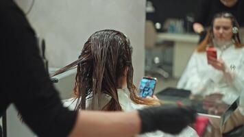 il ragazza usi il Telefono mentre tintura sua capelli con percuras. cura per il aspetto di il dyfstyle bellezza salone, soluzione i problemi durante il bellezza procedura su un' smartphone. alto qualità 4k video