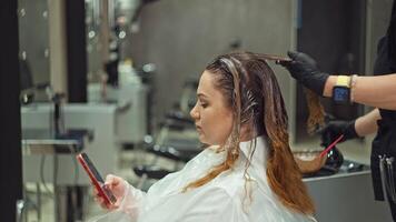 donna d'affari mentre tintura sua capelli nel un' bellezza salone risolve casi su il Telefono. capelli cura nel un' parrucchiere con il Aiuto di un' professionale. alto qualità 4k metraggio video