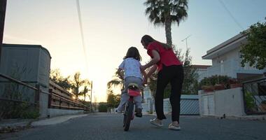 abraçando infância. uma mãe concurso encorajamento Como dela filha leva em a desafio do equitação uma bicicleta, destacando a Função do parental Apoio, suporte e amor dentro aprendizado. Alto qualidade 4k cenas video