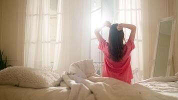 Jeune fille dans le chambre sur le lit redressé sa cheveux et se tenait en haut. le fille juste réveillé en haut. ensoleillé matin, le des rayons faire leur façon par le fenêtre dans le pièce video