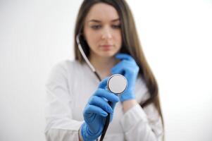 Blur portrait of young alluring nurse with long hair in white medical uniform with focus on stethoscope on neck standing on yellow background copyspace, horizontal picture photo