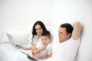 Three man, woman and little boy take selfie in smartphone in bed photo