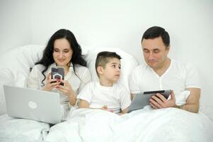 people, family and technology concept happy mother, father and little boy with tablet pc computer in bed at home or hotel room photo