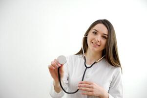 medical university girl student learns to use a phonendoscope correctly she holds in her hands examines smiling in a white coat on a white background training future doctor Be H3althy photo