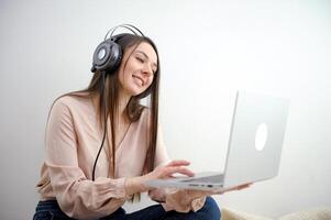 cámara despacio hace zoom en en cara alegre caucásico mujer en auriculares teniendo en línea llamada en computadora portátil, sentado en silla milenario dama participativo en seminario web, comunicado remotamente en Internet foto