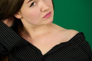 Portrait of the young attractive woman woman on a green background chromakey in a black striped mens shirt different emotions facial expression close-up advertising space for text clean. kind eyes photo