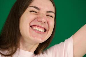 A pretty women throws her head back in a big laugh. different emotions of a young girl on a green background chromakey beautiful facial features real people pink T-shirt white skinned. European photo