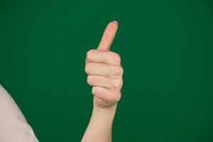 Closeup of female hand showing thumbs up sign against body parts of a young woman on a green background chromakey photo