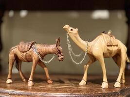 Two sculptures of a donkey and a camel, two wooden sculptures, stand opposite each other on a wooden shelf. They look at each other, each of them has a chain around their neck. photo