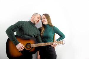 sonriente hermoso hombre mirando a hermosa Novia jugando guitarra aislado en blanco joven Pareja participación manos sentado jugando guitarra foto