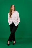 Vertical portrait of a pretty beautiful girl, a happy young woman manager in a jacket and black pants on a green background in studio. Smiling, showing emotions. photo