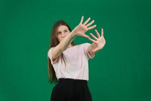 Image of displeased young blond woman defending herself from bright light, raising hands and grimacing bothered, asking to stop taking pictures of her, standing over green background photo