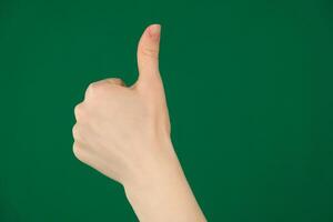Closeup of male hand showing thumbs up sign against green background photo