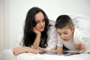 boy, And his mother is working on a laptop computer, The little boy put the tablet in his hand and turned to his busy mother intently, wanting his mother to pay attention to him. photo