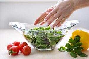 female hands toss a salad in a glass plate to the top next to there are tomatoes pepper and cilantro colorful leaves for cooking diet vegetarian food Cherry tomatoes photo