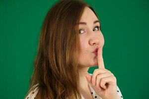 girl put a finger to her lips shows quietly on a green background chromakey concept of silence Be silent Wait carefully Young female expressing emotions in the studio photo