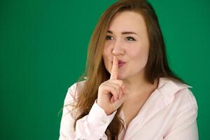 Young girl making silence gesture on green background photo