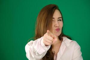 young pretty latin woman smiling with a positive, successful, happy attitude pointing to the camera, making gun sign with hands against green wall photo