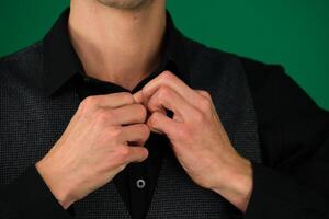 close-up photo of the hands of a man in a black shirt, buttoning up a button on green background