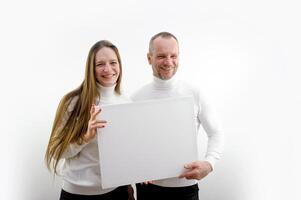 adult man and a young woman holding a picture in their hands a frame for advertising text smiling sincere laughter white clothes white background place empty frame paper cardboard poster banner photo