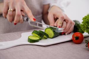 Loving mother teaches daughter to cook vegetable salad, little girl in apron holds knife cutting cucumber on wooden board mom look feel proud share family recipes and experience, pastime hobby concept photo