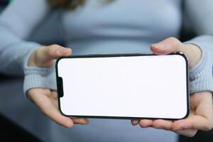 genial móvil oferta. dama señalando dedo a teléfono inteligente emocionalmente reaccionando a nuevo aplicación, teléfono con un blanco pantalla en manos en el gimnasio de cerca gris ropa con largo mangas publicidad espacio para texto foto